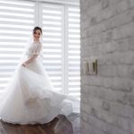 smiled pretty bride is turning around room near white brick wall dressed fashionable dress wedding fashion scaled e1628567673966